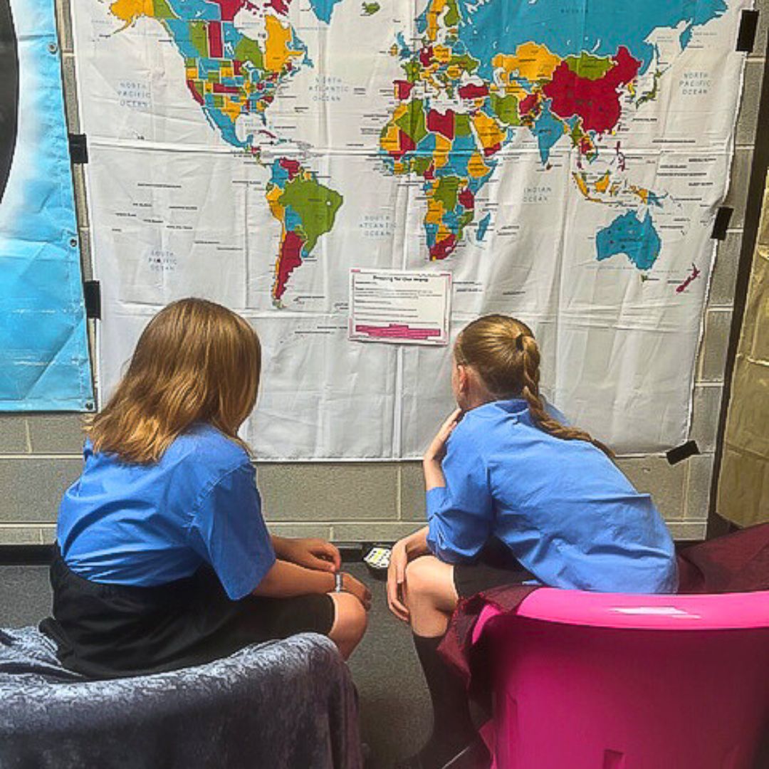 Two school girls sat in a classroom looking at an atlas