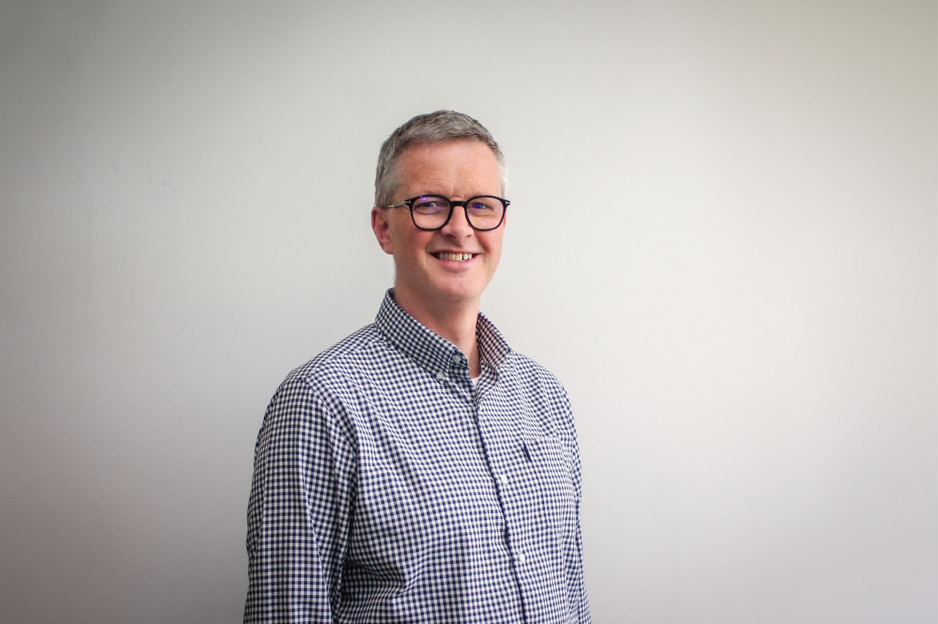 Mat Ineson in a chequered shirt in front of plain backdrop