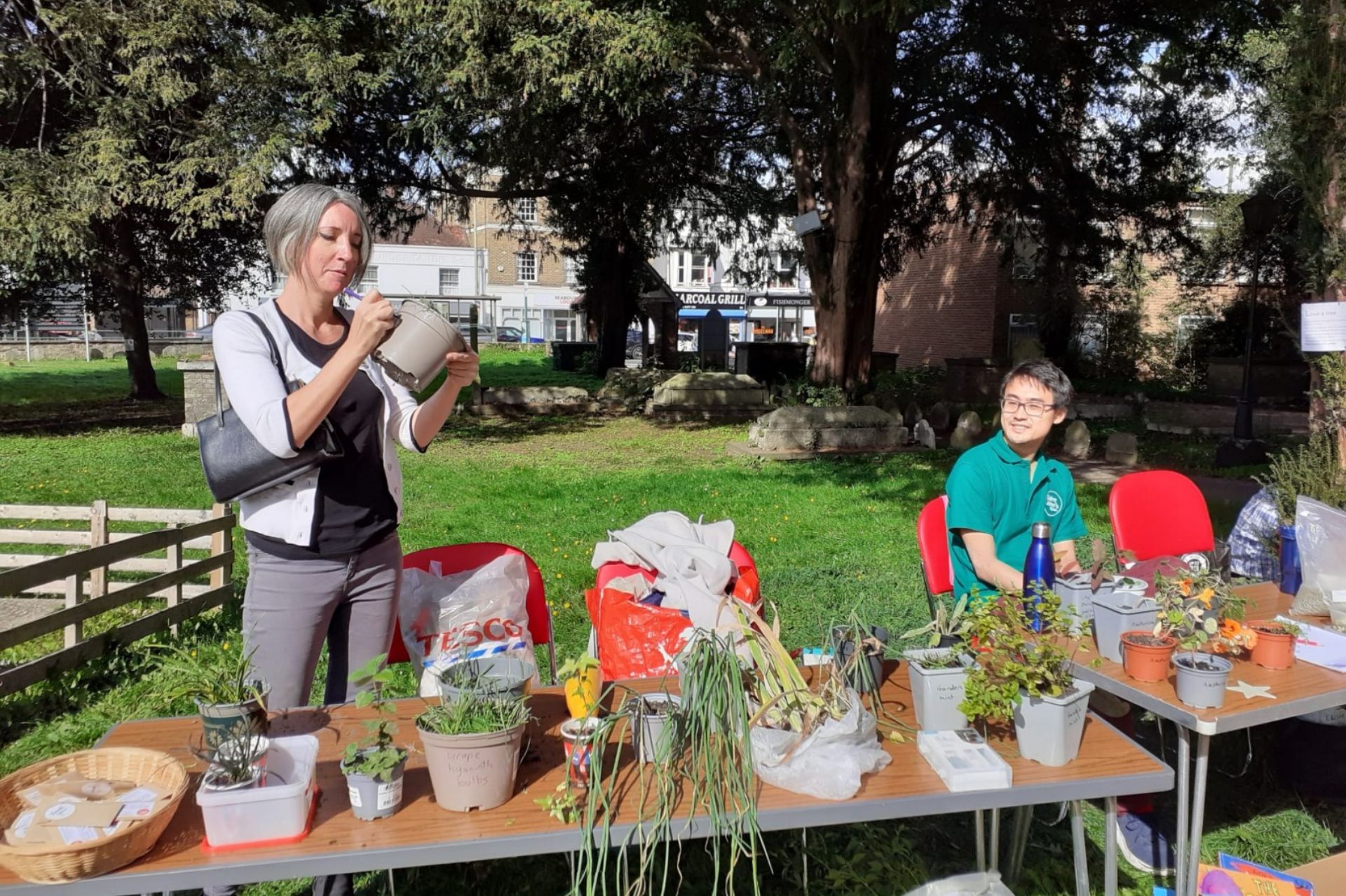 A women stood inspecting a plant pot behind a table of plants